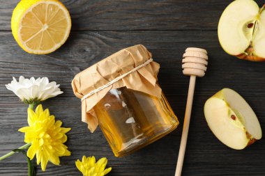 Dipper, apple, lemon, flowers and jar with honey on wooden backg