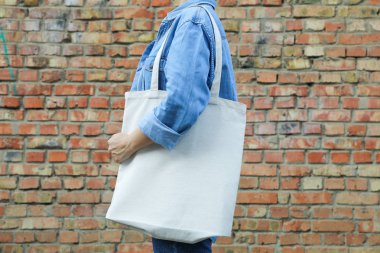 Genç kadın tuğla duvara karşı çanta tutan, boş alan