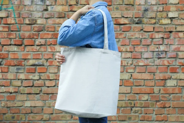 Young woman holding tote bag against brick wall, empty space