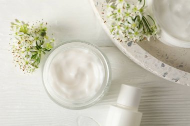 Ahşap arka plan üzerinde kozmetik krem, tepsi ve allium çiçekler,