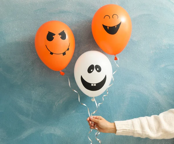 Female hand holding halloween balloons on color background