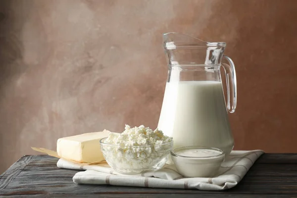 Leite, queijo cottage e manteiga na mesa de madeira contra a ba marrom — Fotografia de Stock