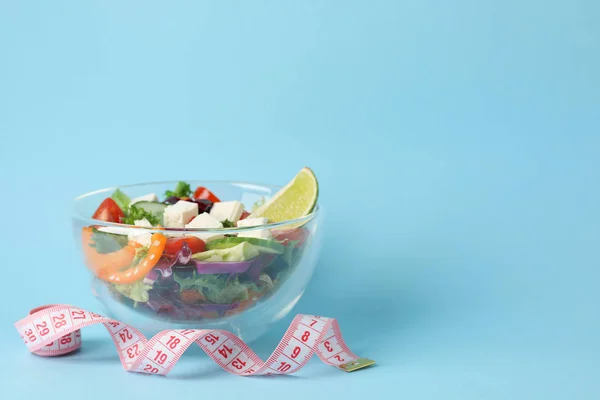 Glass bowl with fresh salad and measuring tape on blue backgroun — Stock Photo, Image