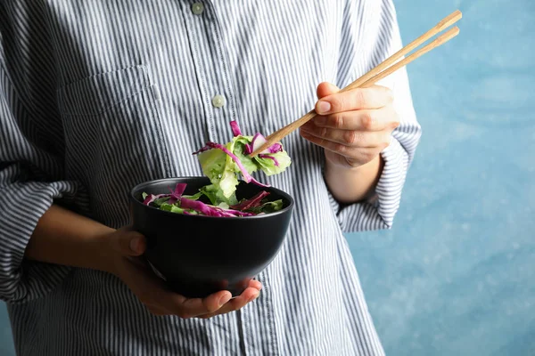 Jonge vrouw eet salade met stokjes op blauwe achtergrond, ruimte — Stockfoto