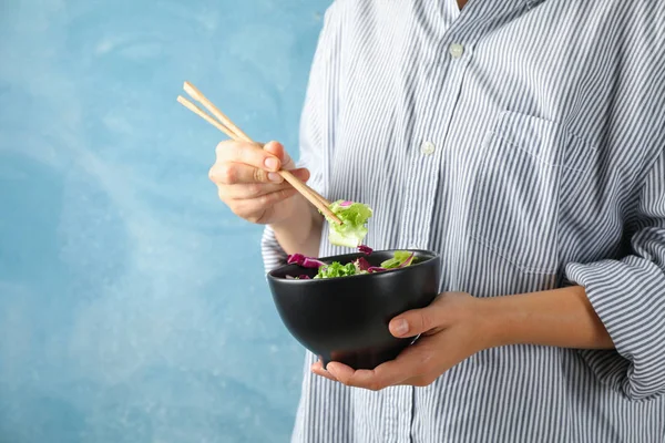Young woman eat salad with chopsticks on blue background, space