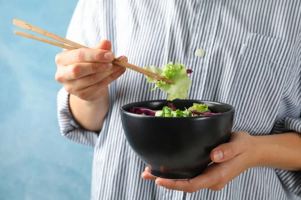Jonge vrouw eet salade met stokjes op blauwe achtergrond, ruimte — Stockfoto