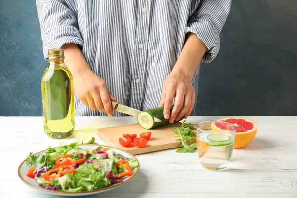 Jonge vrouw plakjes komkommer voor salade op houten achtergrond — Stockfoto