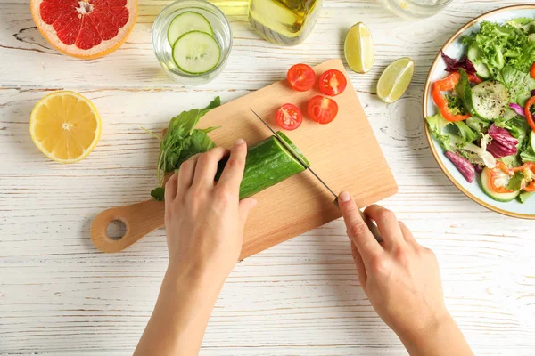 Jonge vrouw plakjes komkommer voor salade op houten achtergrond, Top — Stockfoto