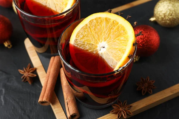 Glasses of tasty mulled wine and christmas baubles on black back — Stock Photo, Image