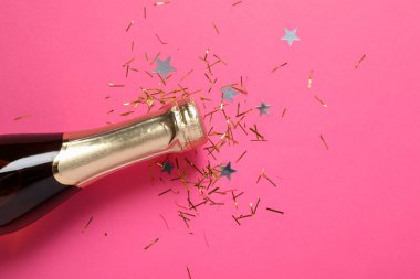 Şampanya şişesi ve pembe arka planda parıltı, yakın plan.