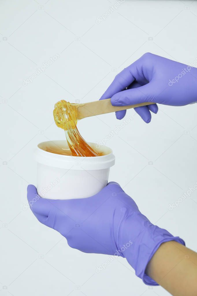 Women's hands holding liquid yellow paste for shugaring against 