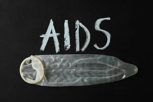 Kondom dan prasasti AIDS pada latar belakang hitam, spasi untuk teks — Stok Foto