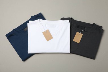 Folded blank t-shirts with tags on gray background, space for te