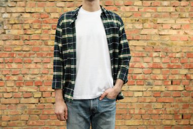 Men in white t-shirt and checkered shirt against brick wall, cop