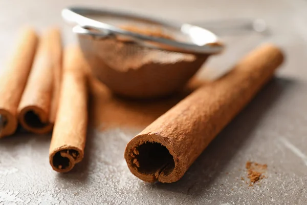 Cinnamon sticks, powder and sieve on grey background, space for — Stock Photo, Image