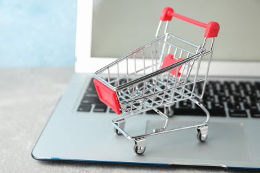 Small shopping cart and laptop on grey background, copy space