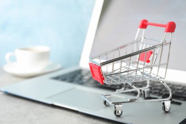 Shopping cart, cup of coffee and laptop on grey background, copy
