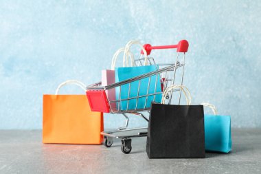 Small shopping cart and paper bags on grey background, copy spac