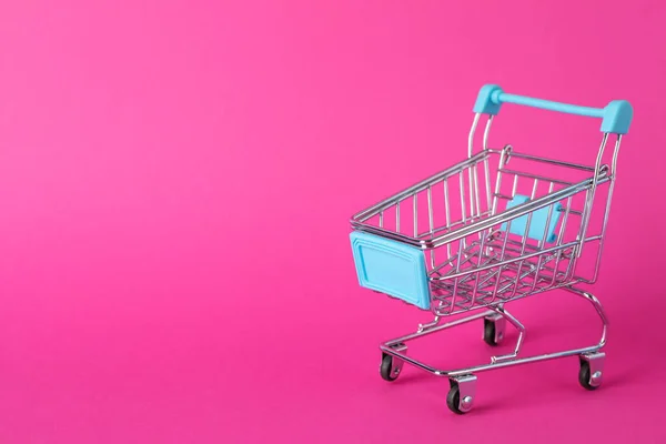 Small shopping cart on pink background, space for text — Zdjęcie stockowe