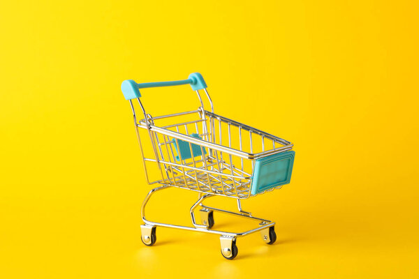 Small shopping cart on yellow background, space for text