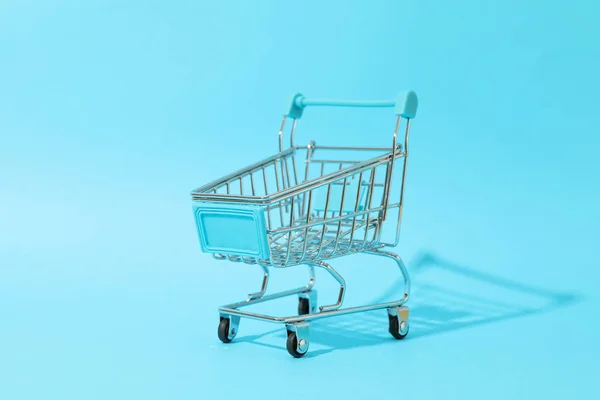 Small shopping cart on blue background, space for text — ストック写真