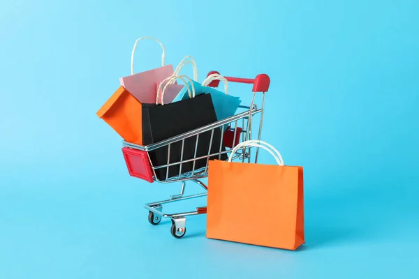 Small shopping cart with paper bags on blue background, space fo — ストック写真