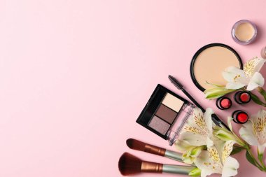 Farklı makyaj malzemeleri ve pembe arka planda çiçekler. Kadın aksesuarları