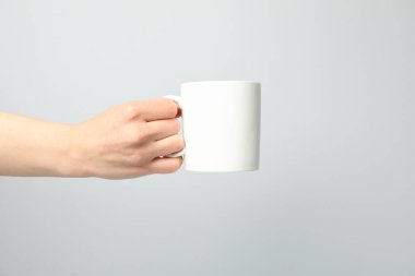 Açık gri zemin üzerinde beyaz bardak tutan kadın el, metin için boşluk