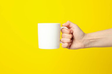 Sarı zemin üzerinde beyaz bardak tutan kadın el, metin için boşluk