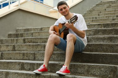 Genç adam basamaklarda oturur ve gitar çalar.