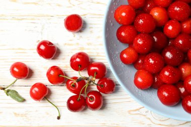 Beyaz ahşap zemin üzerinde kırmızı kiraz tabağı, üst görünüm