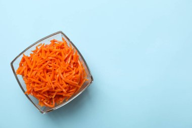 Mavi arka planda havuç salatası olan bir kase.