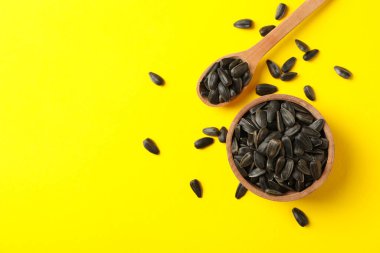Sarı arka planda ayçiçeği tohumları olan kase ve kaşık.