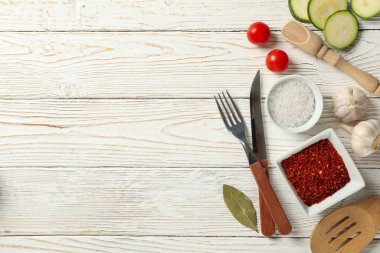 Mutfak çatal bıçak takımı ve beyaz ahşap arka planda yemek pişirmek için malzemeler, üst manzara.