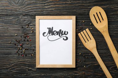 Metin menüsü ve ahşap zemin üzerinde çatal bıçak takımı olan çerçeve