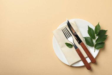 Bej arka planda peçete, çatal bıçak ve yaprak, üst görünüm.