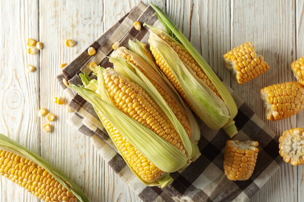 Fresh raw corn and napkin on white wooden background, top view