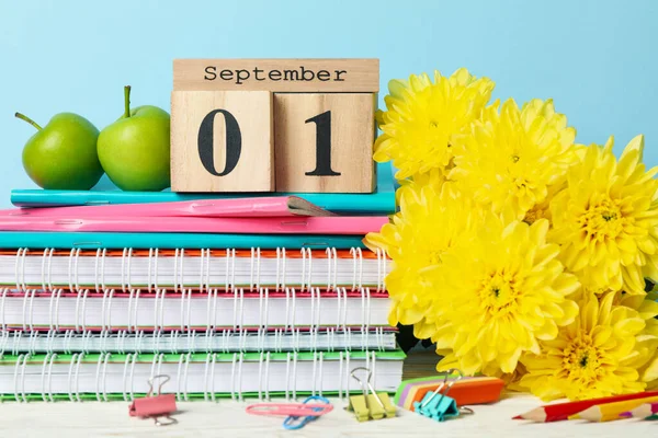 Wooden calendar with 1 september and school supplies on blue background, close up
