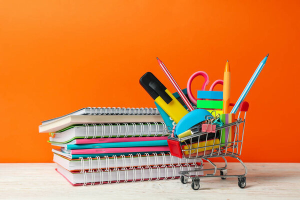 Shopping trolley with school supplies on orange background, space for text