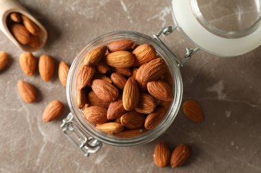 Tahta kepçe ve gri masada badem bulunan cam kavanoz. Vitamin yiyeceği.