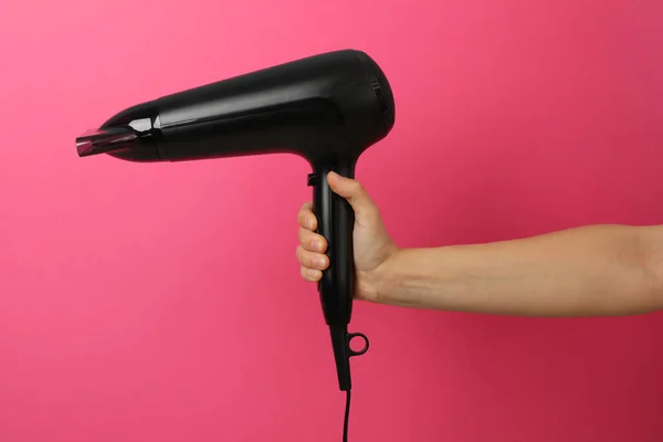 Female hand holds hair dryer on pink background, space for text