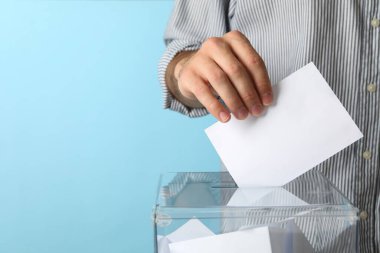 Mavi arkaplana karşı oy sandığına oy veren adam