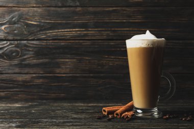 Bir bardak kahve, kahve tohumu ve ahşap arka planda tarçın.