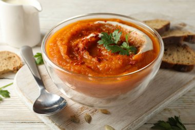 Beyaz ahşap zemin üzerinde bir kase balkabağı çorbası ile kompozisyon, yakın