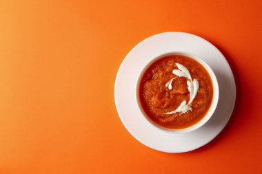 Turuncu arka planda bir kase kabak püresi.