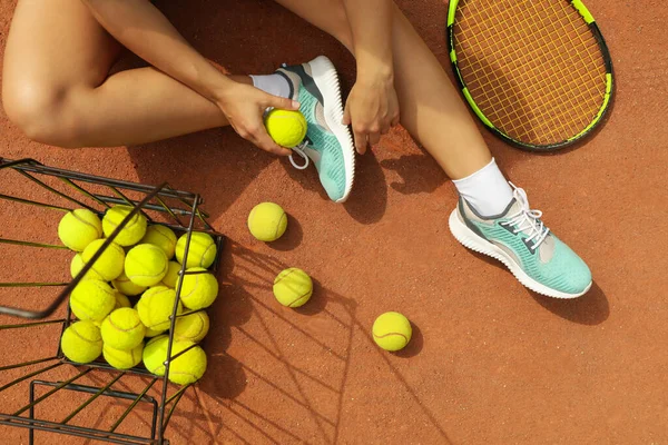 Woman hold tennis ball on clay court with racket and balls