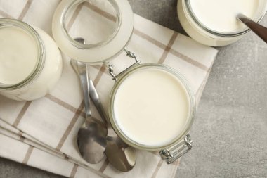 Cam kavanozlar dolusu yoğurt, kaşıklar ve gri arka planda peçete.