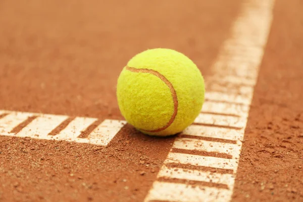 Light green tennis ball on clay court, close up