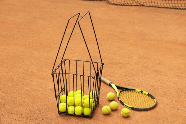 Racket and basket with balls on clay court