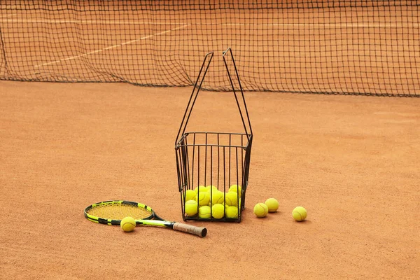 Racket and basket with balls on clay court